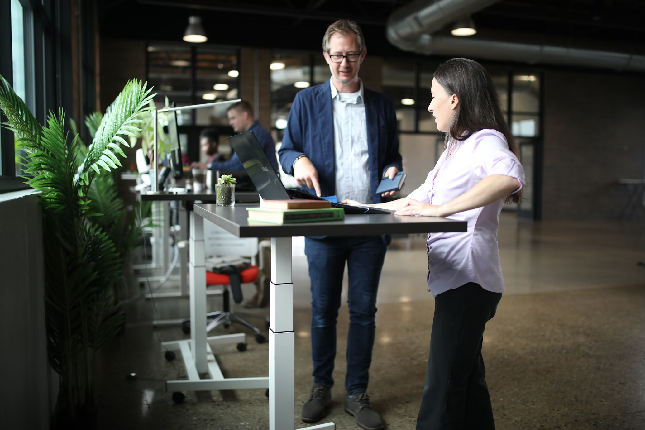 Deux collaborateurs échangeant devant un poste de travail en open space